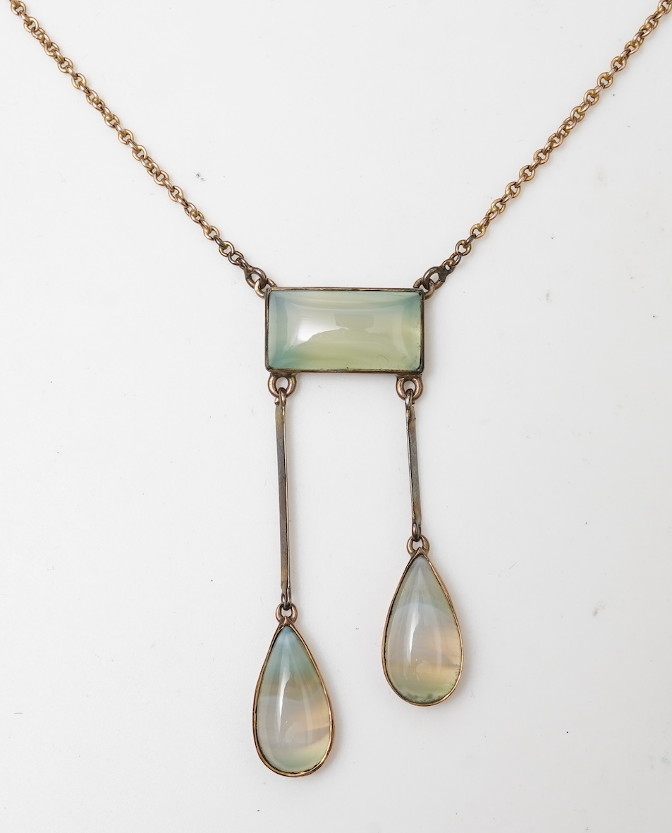 An Edwardian agate necklace, early 20th century, of negligée design, centring on a rectangular cabochon of translucent pale green agate, suspending a pair of pendants of unequal lengths, culminating in pear-shaped caboch